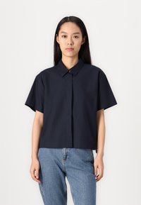 Camisa de botones de manga corta en navy con cuello, hecha de tejido suave. Presenta un corte recto y detalles de costura sutiles.