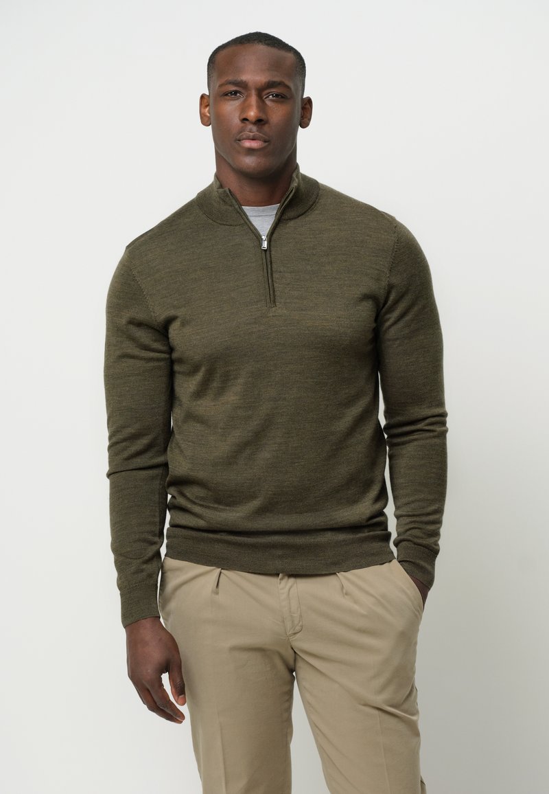 Olivgrüner Strickpullover mit einem Viertel-Reißverschlusskragen, langen Ärmeln und gerippten Bündchen. Über einem hellgrauen Hemd getragen, kombiniert mit beigen Hosen.