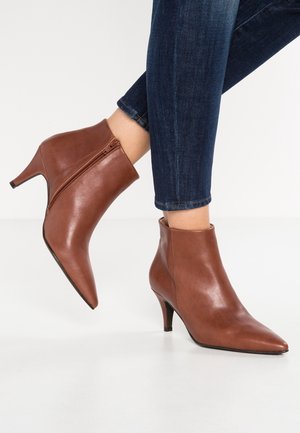 Bottines en cuir marron avec fermetures éclair latérales et petits talons aiguilles portées avec un jean skinny bleu foncé.