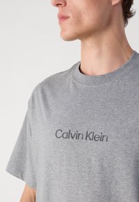 Grå bomull t-skjorte med rund hals og korte ermer, med "Calvin Klein" brodert i en mørkere gråfarge foran.