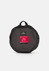 Zwarte netten sporttas met een ronde vorm. Bevat dubbele handvatten, een rood label en een rits. Getextureerd oppervlak met zichtbare stiksels.