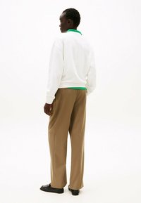 Witte sweatshirt met een groene kraag, gecombineerd met bruine wijde broek en zwarte schoenen. De textuur lijkt soepel en ontspannen.