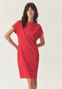Robe rouge avec un décolleté drapé et des manches courtes, présentant une silhouette ajustée qui tombe juste au-dessus du genou.