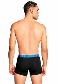 Boxer neri con una fascia in blu con il logo Puma, design aderente, materiale in cotone, visto da dietro. Texture liscia e forma semplice.
