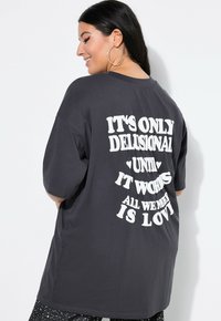 Ciemnoszara, oversize t-shirt z krótkim rękawem, z odważnym białym napisem na plecach w zabawnej typografii i luźnym kroju.