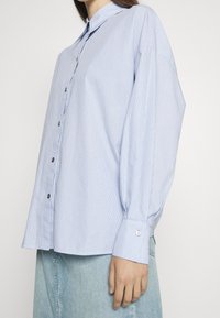 Camicia a righe blu e bianche con colletto classico, maniche a cuffia e vestibilità rilassata, realizzata in tessuto leggero.
