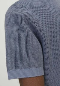 Svetr s krátkým rukávem v světle modré barvě. Má texturovaný žebrovaný vzor a přiléhavé manžety. Materiál se jeví jako měkký s prodyšnou tkaninou.