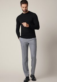 Czarny sweter z długim rękawem, szare spodnie na miarę oraz czarne eleganckie buty. Gładkie materiały, dopasowany krój, z neutralnym tłem.