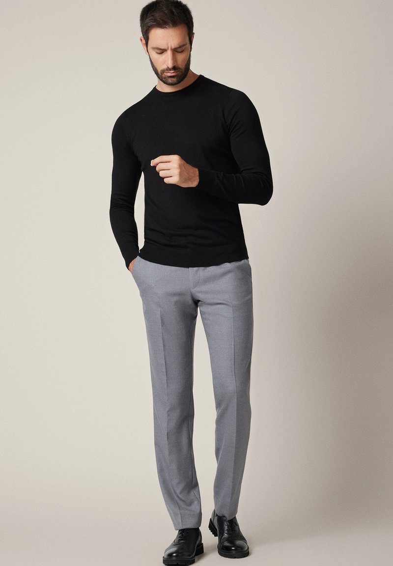 Czarny sweter z długim rękawem, szare spodnie na miarę oraz czarne eleganckie buty. Gładkie materiały, dopasowany krój, z neutralnym tłem.