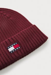 Maroon knit beanie with ribbed texture, featuring a branded patch with "TOMMY JEANS" and red, white, and blue accents.