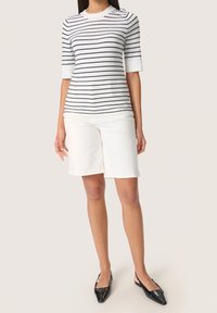 Top de punto a rayas en blanco y azul marino, con mangas cortas, combinado con pantalones cortos color crema hasta la rodilla. La modelo lleva sandalias negras con tacón trasero.