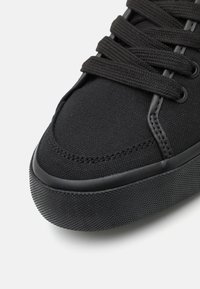 Baskets noires en toile avec lacets plats, semelle en caoutchouc texturé et embout renforcé. Présente des coutures tonales et des œillets en métal pour le laçage.