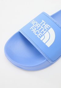 Svetlo modri natikač s teksturirano gumijasto podplato. Ima širok trak, na katerem je v belem napisan logotip "THE NORTH FACE". Gladek, sproščen izgled.