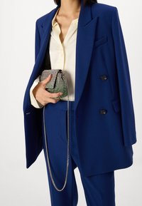 Blå oversized kavaj med skarpa slag, svarta knappar och en glansig handväska med silverkedja som accent. Krämfärgad skjorta med knappar under.