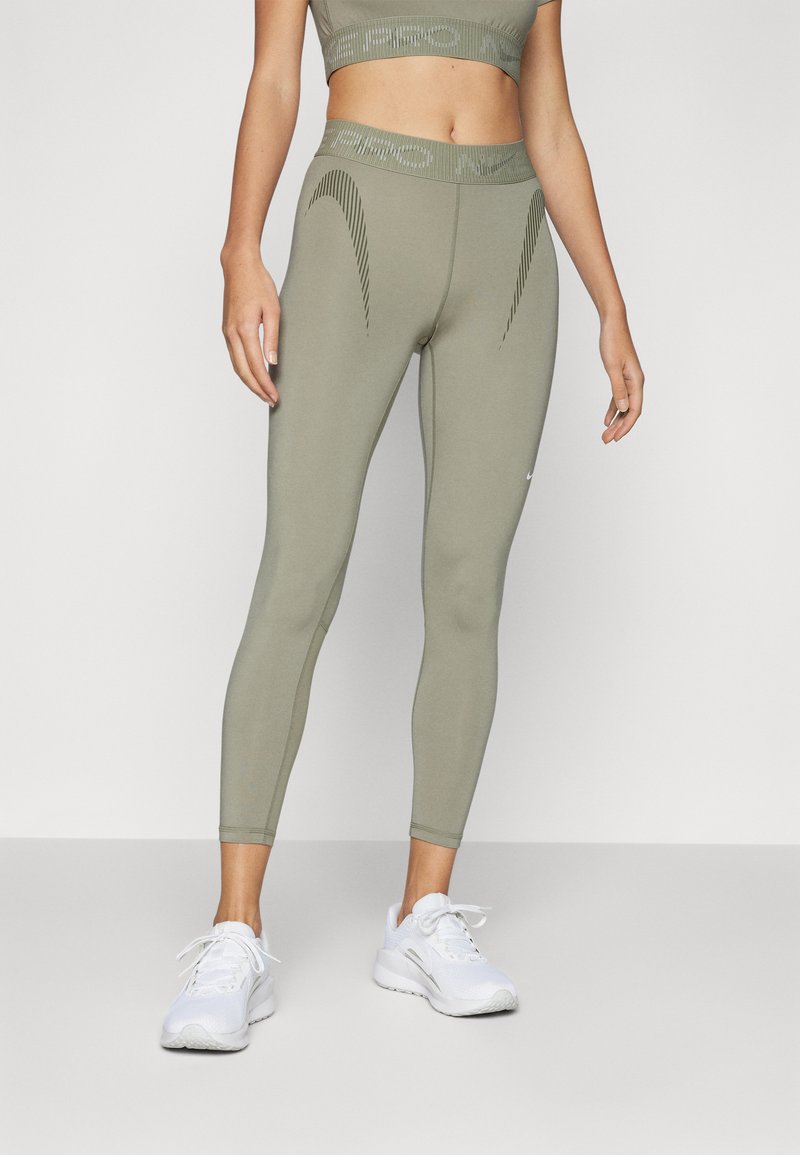 Olivenfargede leggings med teksturert midjebånd, slim passform og buede sømmer. Kombinert med hvite treningssko.