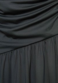 Czarna sukienka z drapowaną tkaniną na górze i marszczonym wykończeniem na dole, podkreślona miękkim, gładkim materiałem.