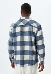 Camicia di flanella a quadri blu e bianca con colletto a punta, maniche lunghe e polsini con bottone. La trama del tessuto appare morbida e calda.