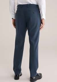 Pantalons ajustés bleu marine avec une texture lisse, dotés de deux poches arrière avec des boutons, et une coupe slim fuselée. Chaussures noires visibles.