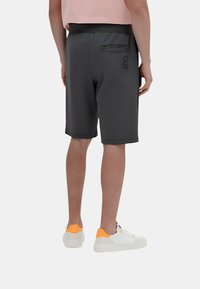 Pantaloni sportivi grigi con una finitura texture, vita elastica e tasca posteriore. Abbinati a scarpe da ginnastica bianche con dettagli arancioni.