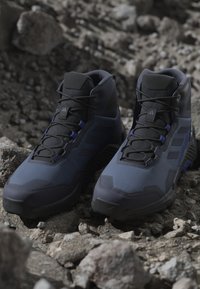 Mörkblå vandringskängor med en strukturerad ovandel, förstärkt tå, svarta snörning och en robust sula, designade för utomhusbruk.