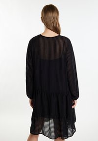 Rochie neagră, din material transparent cu dungi verticale, având mâneci lungi și o croială lejeră, oferind o siluetă fluidă.