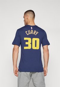 Námořnická modrá sportovní tričko s žlutým nápisem "CURRY" nad číslem "30" na zadní straně, s kulatým výstřihem a krátkými rukávy.
