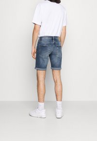 Shorts de mezclilla en azul claro con dobladillos enrollados, que presentan dos bolsillos traseros y una etiqueta de cuero de la marca en la cinturilla. Llevados con zapatillas blancas.