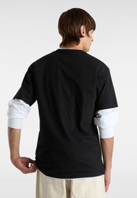Sort bomulds t-shirt med kortærmer over en hvid langærmet skjorte. Har en afslappet pasform og et enkelt design uden yderligere detaljer.