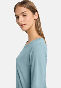 Cămașă lungă cu mâneci, de culoare albastru deschis, cu un decolteu rotund, textură netedă și design minimalistic. Remarcabilă pentru croiala sa lejeră și aspectul elegant.