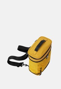 Borsa isolata gialla di forma rettangolare, con chiusura a zip, una tracolla nera e un manico superiore piatto. Presenta un logo sul lato.