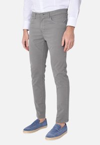 Pantaloni di cotone grigi con vestibilità slim, dotati di cinque tasche, chiusura anteriore con bottone e una texture liscia. Indossati con mocassini blu.