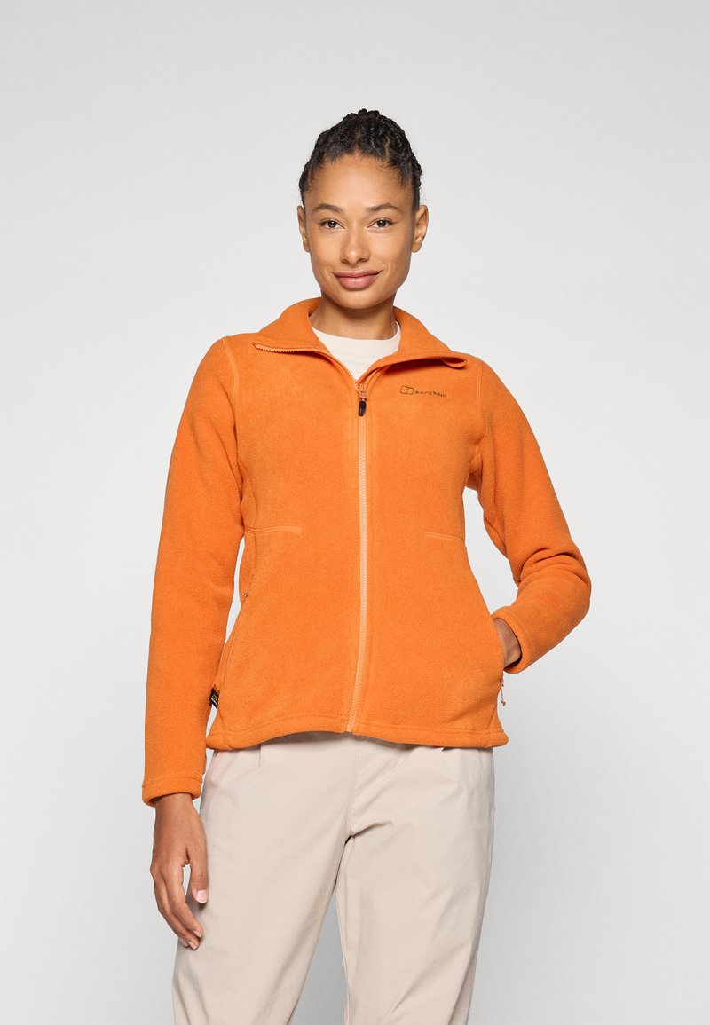 Orangenes Fleece-Jackett mit Reißverschluss, Stehkragen und seitlichen Taschen. Weiche Textur und taillierte Passform, kombiniert mit hellbeigen Hosen.