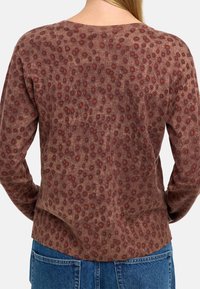 Sweter z długim rękawem w teksturowanym brązowym materiale z wzorem czerwonych kropek. Posiada okrągły dekolt i luźny krój.