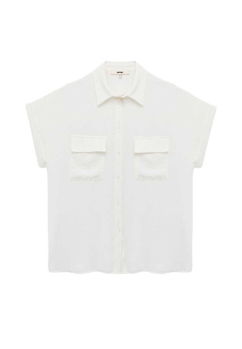 Chemise blanche à boutons avec manches courtes, comportant deux poches avant, une texture douce et un col classique. Détail de l'ourlet festonné.