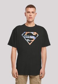 Black cotton t-shirt featuring a large, multi-patterned Superman logo in orange, blue, and white, with a loose fit and short sleeves.