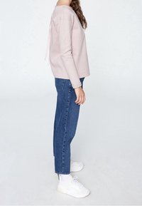 Sweatshirt rose clair avec un col rond et un détail de lien au dos, associé à un jean droit bleu et des baskets blanches.