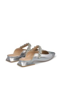 Des chaussures à talons plats argentées à bride arrière, ornées d'accents en cristal décoratifs sur la sangle et d'une finition métallique lisse.