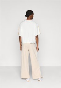 Fehér rövid ujjú felső sárga díszítéssel; bézs színű, széles szárú nadrág oldalsó csíkokkal; könnyű, sima anyag; kényelmes, laza szabás.