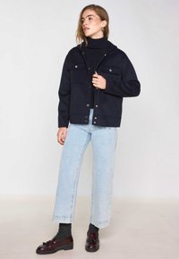 Giacca in misto lana blu navy con due tasche anteriori, chiusure a pressione e vestibilità comoda, abbinata a jeans denim azzurri e mocassini bordeaux.