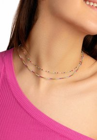 Collar de múltiples hilos con acentos de cuentas coloridas, que presenta una mezcla de colores pastel y brillantes sobre una cadena en tono dorado, descansando sobre la piel.