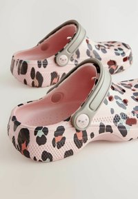Klumpy s leopardím vzorom s ružovým podkladom, šedým popruhom a textúrovanou podrážkou. Obsahujú ventilačné otvory a gombík s dizajnom mačky.