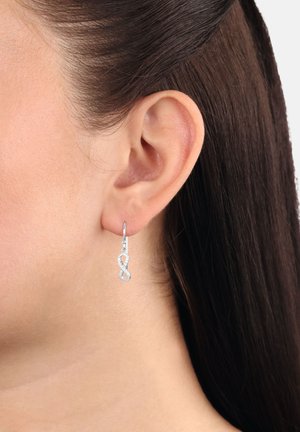 Orecchini a cerchio in argento a forma di simbolo dell'infinito, con una finitura lucida e dettagli testurizzati, indossati all'orecchio di un modello.