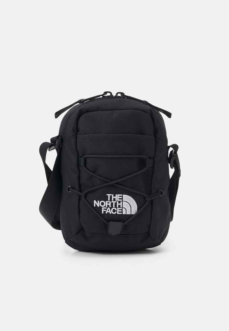 Mała czarna torebka na ramię z regulowanym paskiem, przednim sznurkiem bungee i białym logo "The North Face" na przedniej kieszeni.