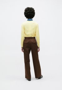 Κίτρινο πουλόβερ με υφή πλεκτού και μανσέτες με πράσινες και λευκές ρίγες, σε συνδυασμό με καφέ παν τελόνι φαρδιάς γραμμής με τσέπες στο πίσω μέρος.