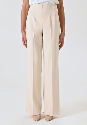 Beige, hoge taille broek met een rechte pijpdesign, gekenmerkt door scherpe plooien en een gladde textuur. Gecombineerd met nude topjes met een spitse neus.