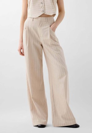 Pantaloni beige a gamba larga con sottili righe verticali, dotati di tasche frontali e un taglio sartoriale. Realizzati in un tessuto leggero.