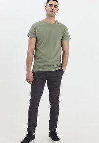 Camiseta de algodón color verde oliva con cuello redondo, usada con pantalones de chándal ajustados en gris oscuro con puños elásticos y zapatillas negras.