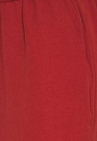 Punainen kangas, jossa on sileä pinta, varustettuna rypytetyllä vyötärönauhalla ja sivutaskuilla. Kankaassa on hienovarainen kudontamalli.