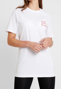 Bílý bavlněný tričko s krátkým rukávem, na přední straně s červeným grafickým textem "už mi chybí léto".