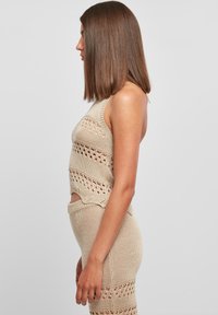 Top sin mangas de punto beige con corte lateral y patrones de puntos abiertos, combinado con una falda ajustada a juego que presenta diseños similares.